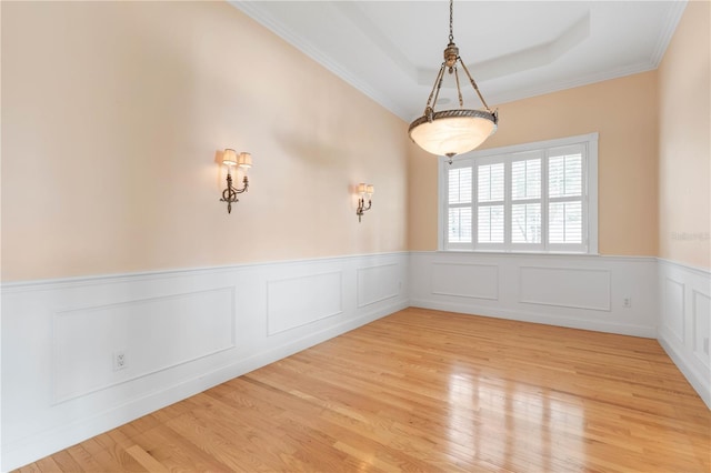 empty room featuring light wood-type flooring, a tray ceiling, and crown molding