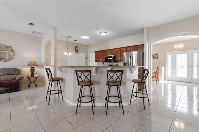 kitchen with appliances with stainless steel finishes, light stone counters, a breakfast bar, a notable chandelier, and hanging light fixtures