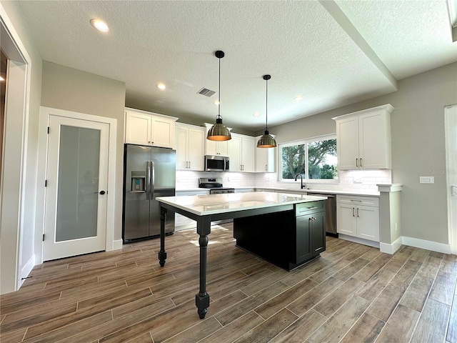 kitchen featuring a kitchen island, white cabinetry, hanging light fixtures, and appliances with stainless steel finishes