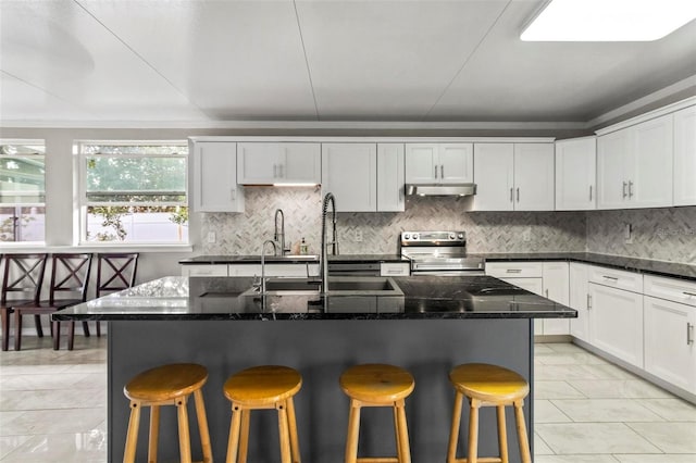 kitchen with stainless steel range with electric cooktop, a kitchen breakfast bar, and an island with sink