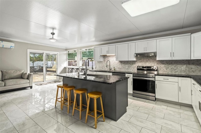 kitchen featuring electric range, a kitchen island with sink, an AC wall unit, sink, and white cabinetry