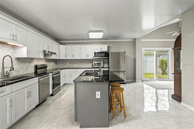 kitchen with a breakfast bar area, appliances with stainless steel finishes, an island with sink, sink, and backsplash