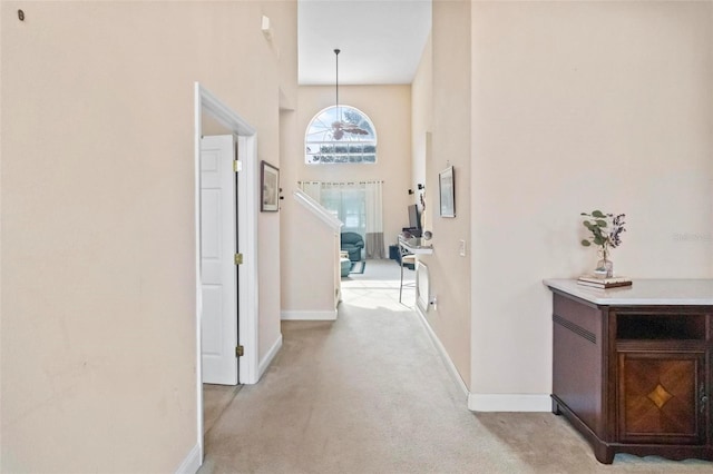 hallway featuring light colored carpet and a towering ceiling