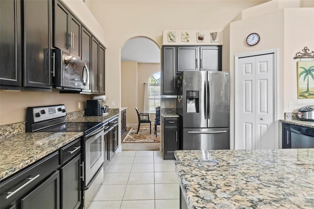 kitchen featuring appliances with stainless steel finishes, light stone counters, dark brown cabinetry, and light tile patterned floors