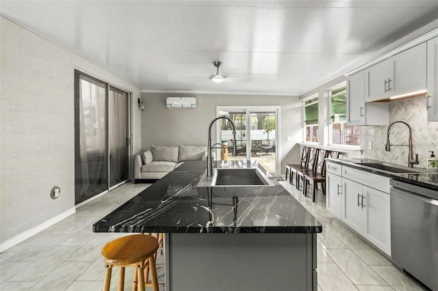 kitchen with stainless steel dishwasher, a center island with sink, sink, and dark stone counters