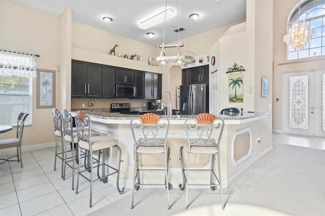 kitchen featuring light stone countertops, hanging light fixtures, stainless steel appliances, light tile patterned floors, and a kitchen bar