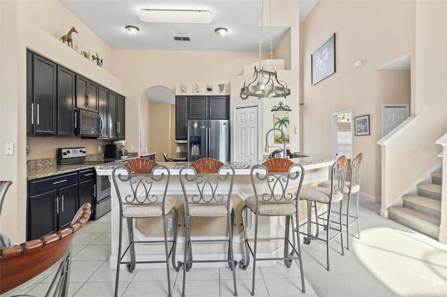 kitchen with appliances with stainless steel finishes, light stone countertops, a kitchen bar, decorative light fixtures, and light tile patterned flooring