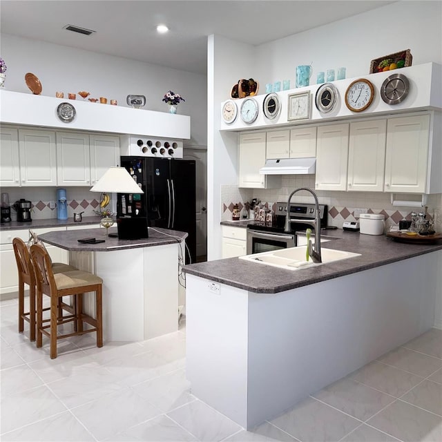 kitchen featuring decorative backsplash, a kitchen island with sink, electric stove, light tile patterned floors, and a breakfast bar area