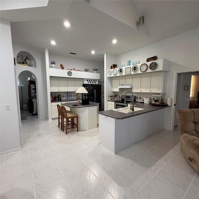 kitchen with black refrigerator, a kitchen breakfast bar, kitchen peninsula, stainless steel range with electric stovetop, and a kitchen island