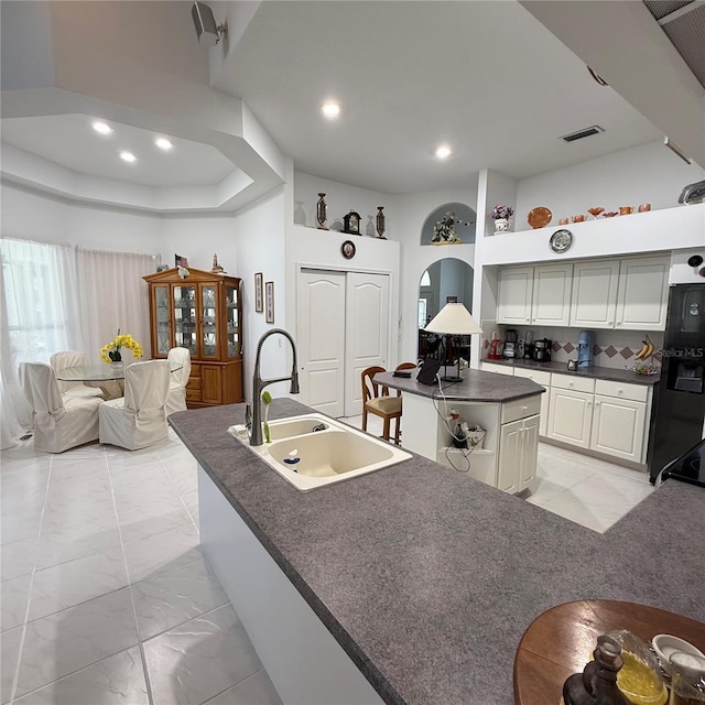 kitchen featuring black fridge with ice dispenser, backsplash, a kitchen island with sink, and sink