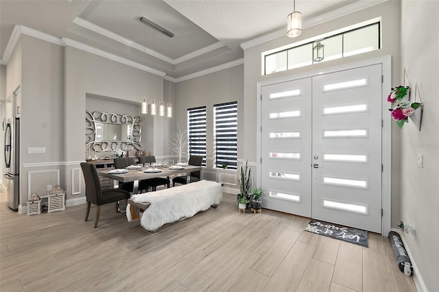 entryway with light hardwood / wood-style floors, a raised ceiling, and crown molding