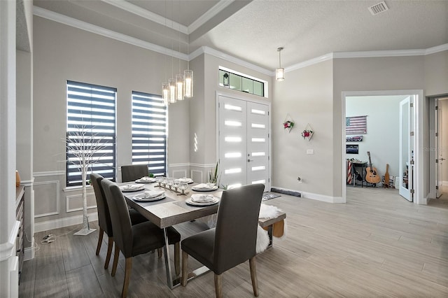 dining room with a chandelier, a textured ceiling, light wood-type flooring, and crown molding