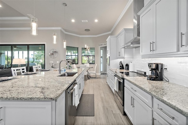 kitchen with sink, wall chimney range hood, decorative light fixtures, white cabinets, and appliances with stainless steel finishes