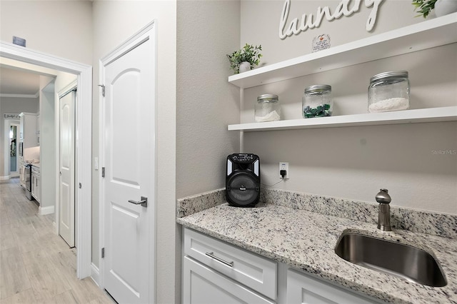 bar with white cabinetry, light wood-type flooring, light stone countertops, and sink