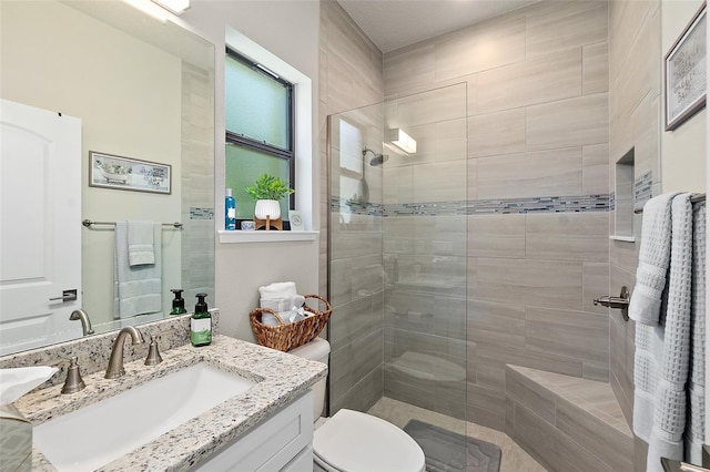 bathroom with a tile shower, vanity, and toilet