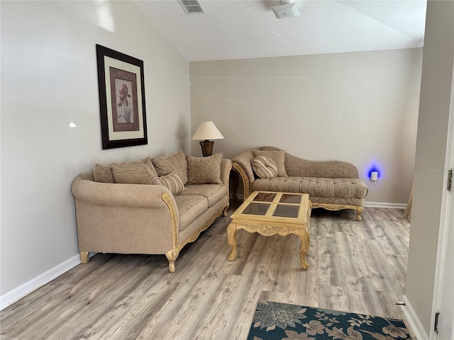 living area with lofted ceiling, wood finished floors, baseboards, and a textured ceiling