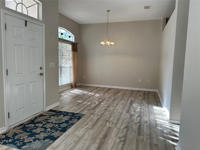 entrance foyer featuring baseboards, wood finished floors, visible vents, and a chandelier