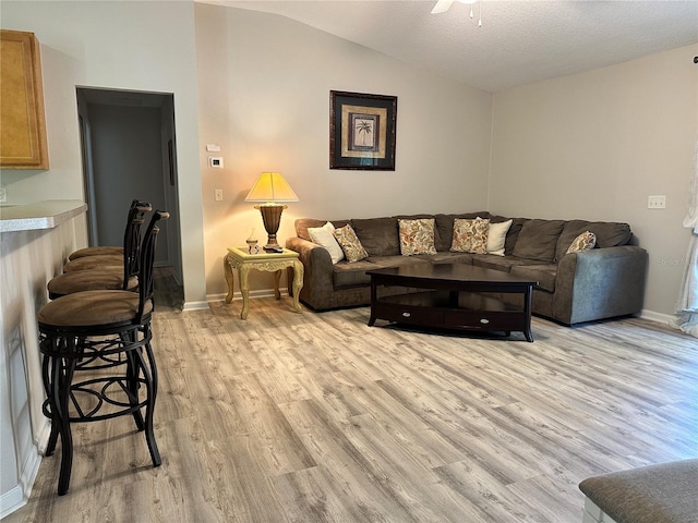 living area featuring baseboards, lofted ceiling, light wood-style floors, and a ceiling fan