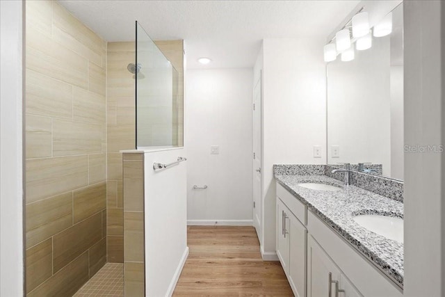 bathroom with hardwood / wood-style floors, vanity, and a tile shower