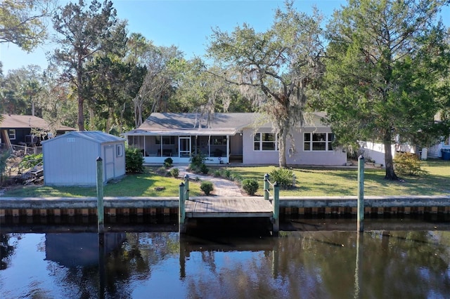 back of house featuring a sunroom, a water view, a yard, and a shed