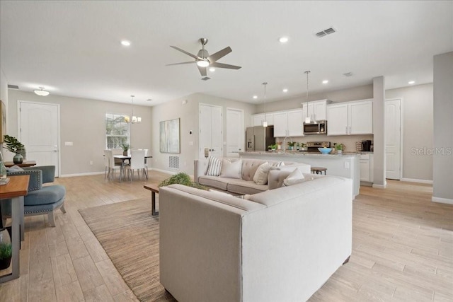 living room with ceiling fan with notable chandelier and light hardwood / wood-style floors