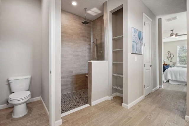 bathroom featuring hardwood / wood-style floors, toilet, ceiling fan, and a tile shower