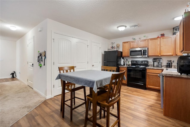 kitchen with black appliances, a textured ceiling, and light hardwood / wood-style floors