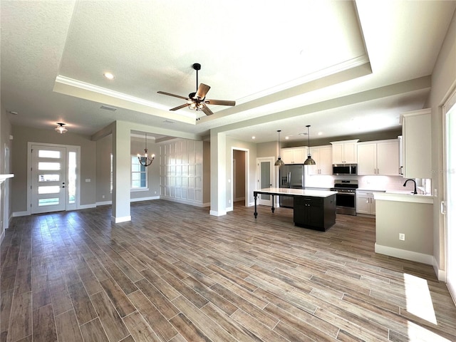 kitchen featuring appliances with stainless steel finishes, a raised ceiling, hardwood / wood-style flooring, white cabinets, and a center island