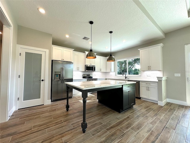 kitchen featuring white cabinets, decorative light fixtures, stainless steel appliances, and a kitchen island