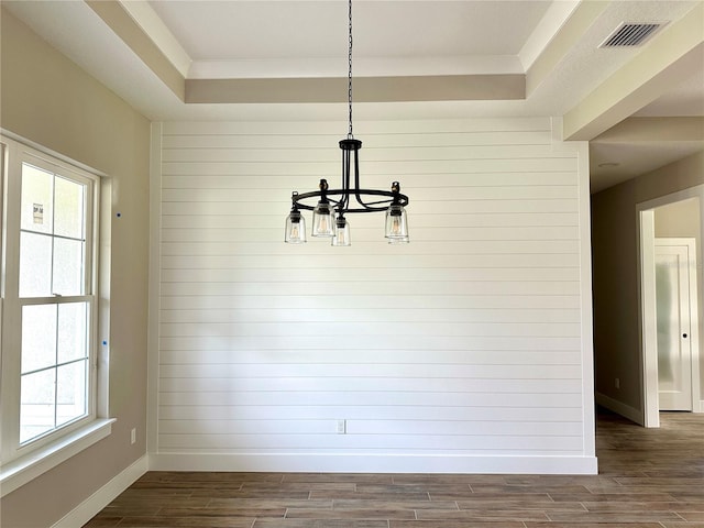 unfurnished dining area featuring a chandelier, a tray ceiling, dark wood-style floors, and baseboards