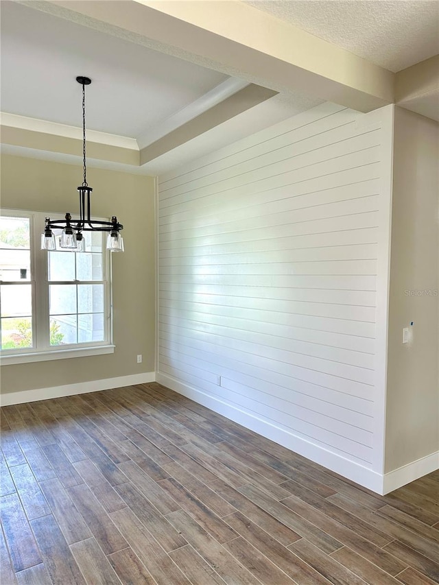 unfurnished dining area with dark wood-type flooring, baseboards, a chandelier, wooden walls, and a tray ceiling