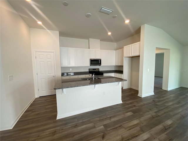 kitchen with dark wood-type flooring, dark stone countertops, a kitchen island with sink, white cabinets, and appliances with stainless steel finishes