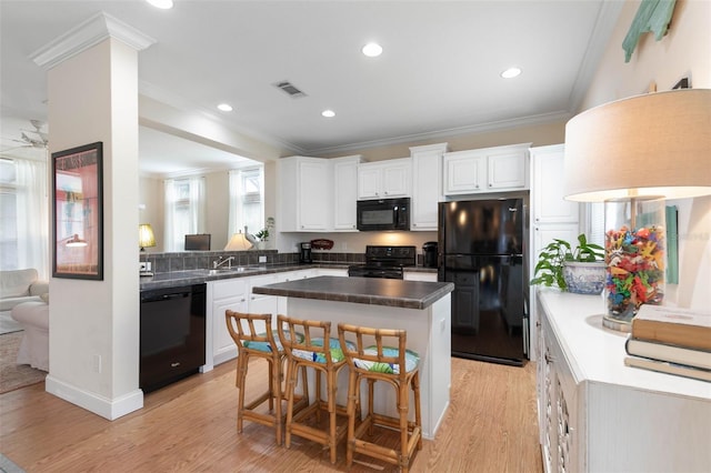 kitchen with a kitchen island, light hardwood / wood-style flooring, white cabinets, black appliances, and ornamental molding