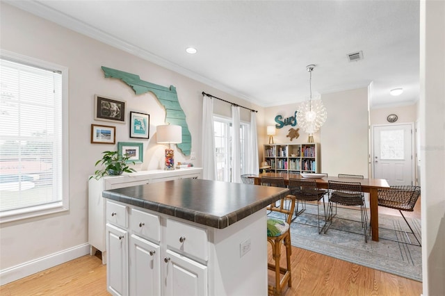 kitchen featuring a kitchen island, crown molding, light hardwood / wood-style flooring, white cabinetry, and hanging light fixtures