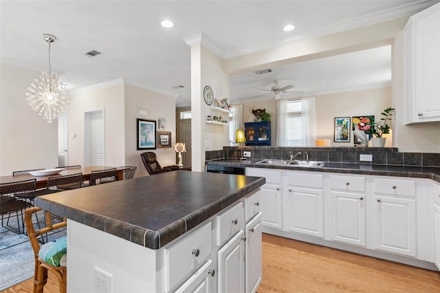 kitchen featuring a center island, sink, hanging light fixtures, white cabinets, and ceiling fan with notable chandelier