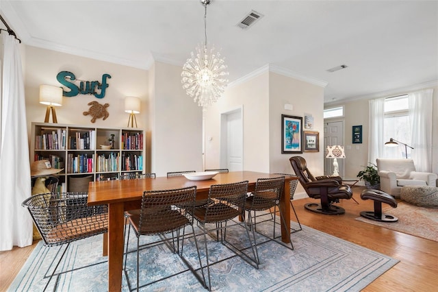 dining space with ornamental molding, light hardwood / wood-style flooring, and an inviting chandelier