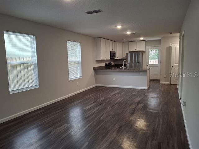 kitchen with appliances with stainless steel finishes, dark hardwood / wood-style floors, sink, white cabinets, and kitchen peninsula