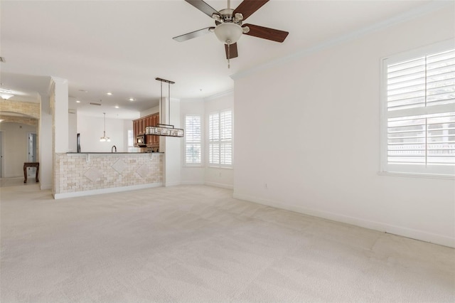 unfurnished living room featuring ceiling fan, ornamental molding, and light carpet