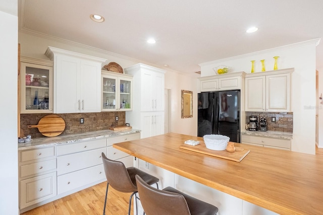 kitchen featuring black refrigerator, decorative backsplash, white cabinetry, and crown molding