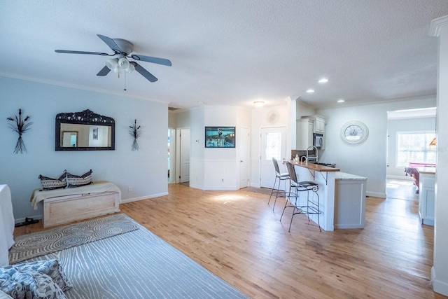 living room featuring sink, ceiling fan, light wood-type flooring, a textured ceiling, and ornamental molding