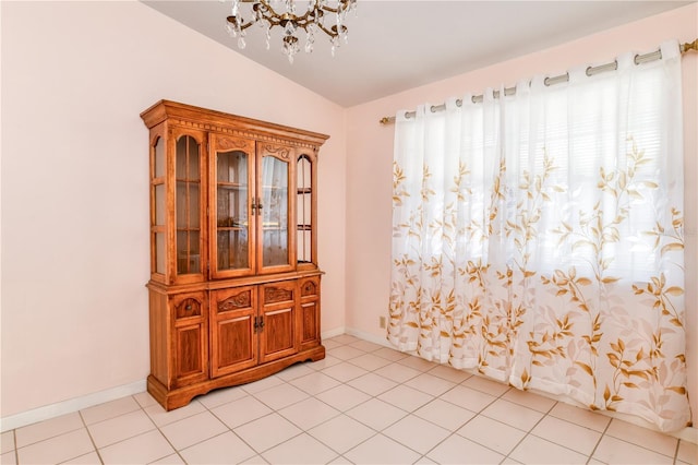 tiled empty room featuring lofted ceiling and an inviting chandelier