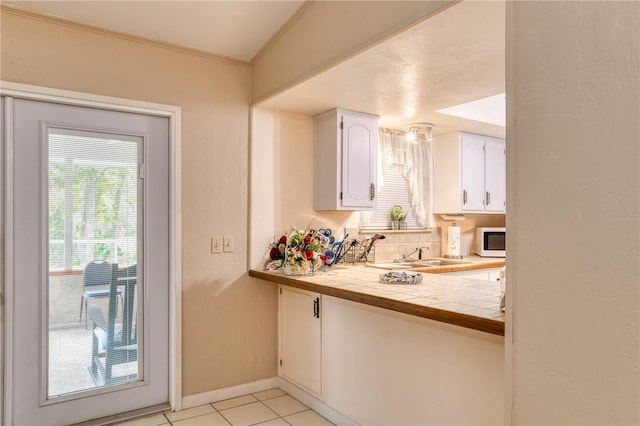 kitchen with crown molding, sink, tile countertops, white cabinetry, and light tile patterned flooring