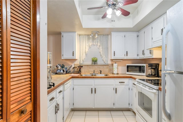 kitchen with a raised ceiling, white cabinetry, sink, and white appliances