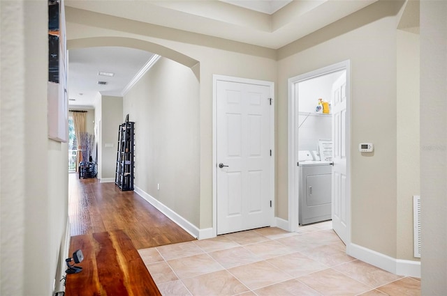 corridor with crown molding, washer and clothes dryer, and light hardwood / wood-style floors