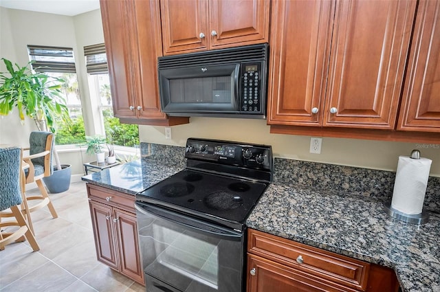 kitchen with black appliances, dark stone countertops, light tile patterned flooring, and brown cabinets