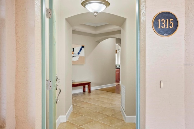 hallway featuring light tile patterned floors, arched walkways, and baseboards