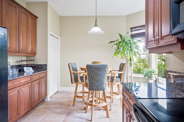 kitchen with light tile patterned floors, hanging light fixtures, dark stone countertops, and brown cabinets