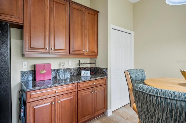 kitchen featuring brown cabinetry, light tile patterned floors, and dark stone counters