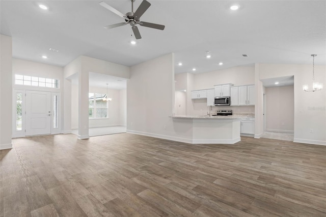 unfurnished living room featuring ceiling fan with notable chandelier, recessed lighting, wood finished floors, and baseboards