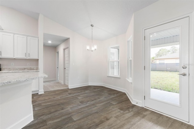 unfurnished dining area featuring a notable chandelier, baseboards, lofted ceiling, and dark wood-style flooring